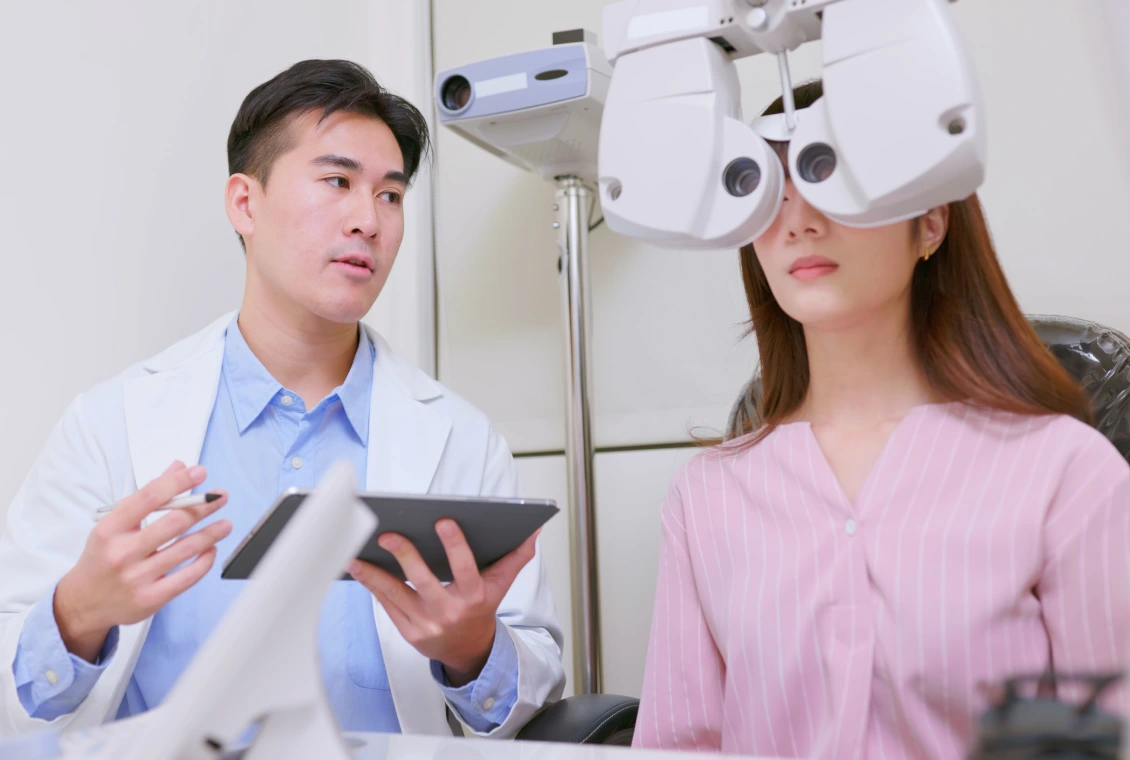 Optometrist examining patient with phoropter machine.