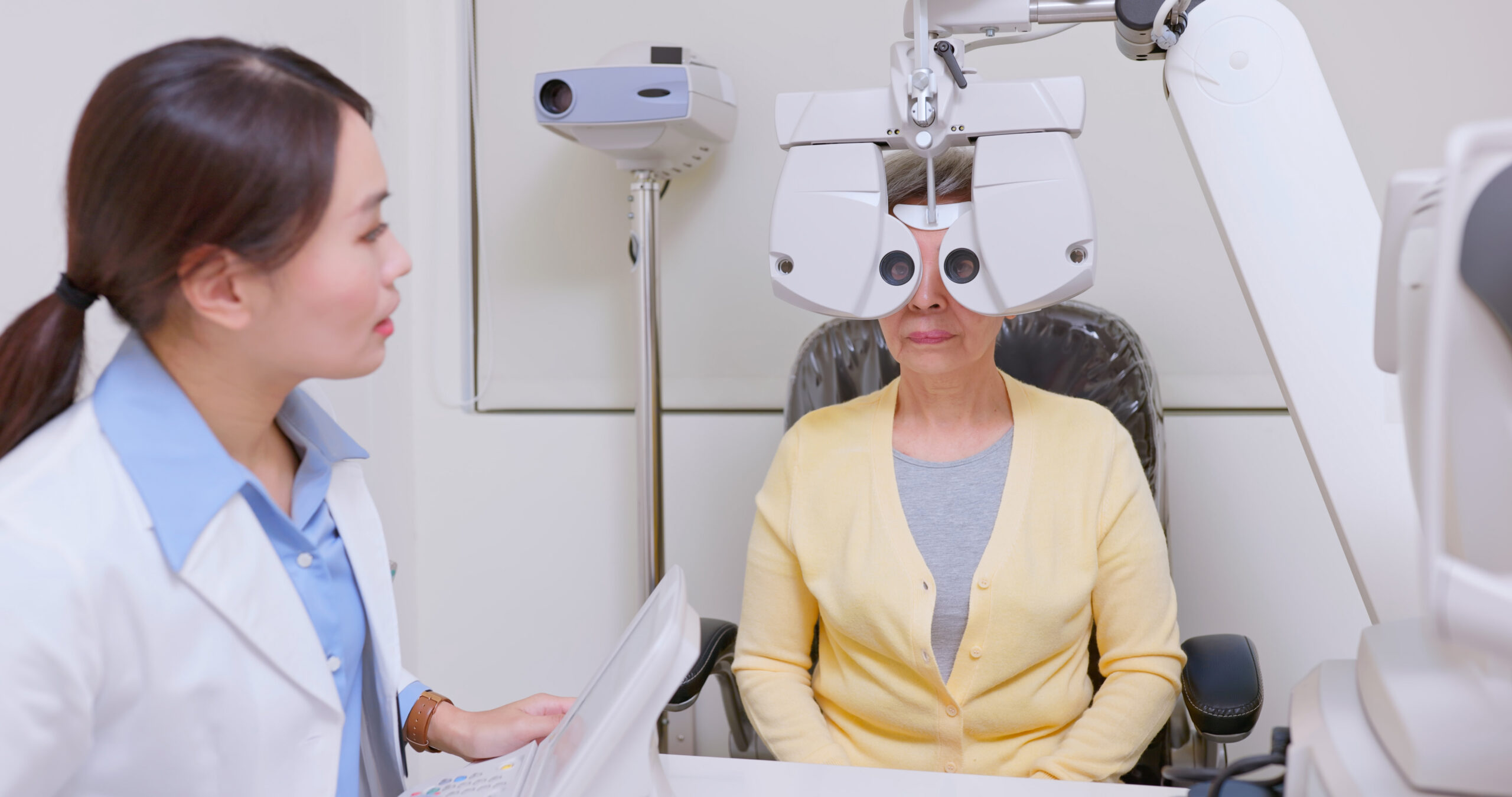 An optometrist prepares to examine a patient's eyes using a phoropter.